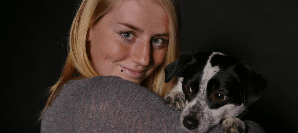 Junge Frau mit Hund im Arm lächelt in die Kamera