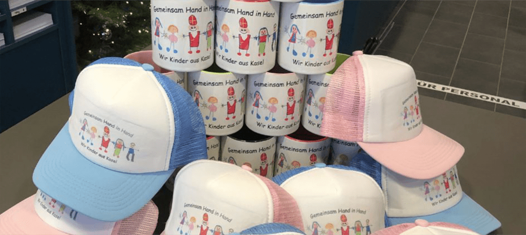 Pyramide aus Caps und Tassen mit aufgedruckter Kinderzeichnung